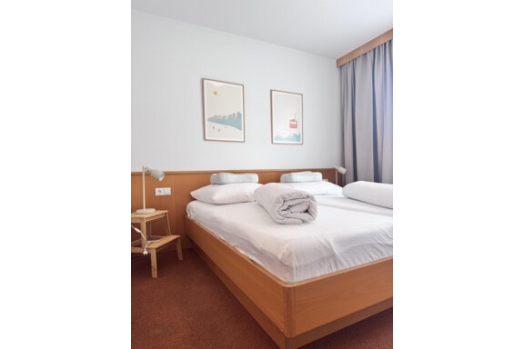 A cozy bedroom with a double bed and fresh, white bedding. Two pictures hang on the wall, and next to the bed stands a modern lamp. - CASA bianco DUE - Sölden