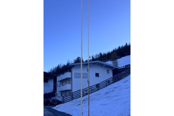 A white building in a snowy landscape, surrounded by coniferous trees. The clear blue sky complements the wintry scene. - CASA bianco DUE - Sölden
