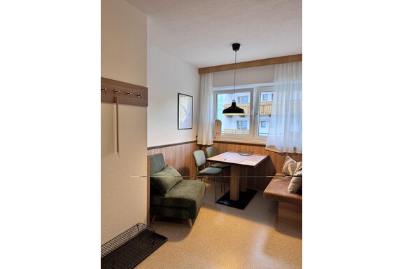 A cozy living space with a table, chairs, and a green armchair. The windows let in plenty of daylight and the wooden paneling creates a warm atmosphere. - CASA bianco DUE - Sölden