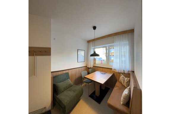 A cozy room with a table, a bench, and a green armchair. Large windows provide plenty of natural light. - CASA bianco DUE - Sölden