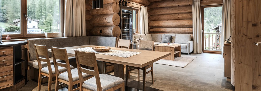 A cozy living space with wooden beams and large windows. A dining table with chairs and a seating area create an inviting atmosphere. - Chalet Resort Sölden - Sölden