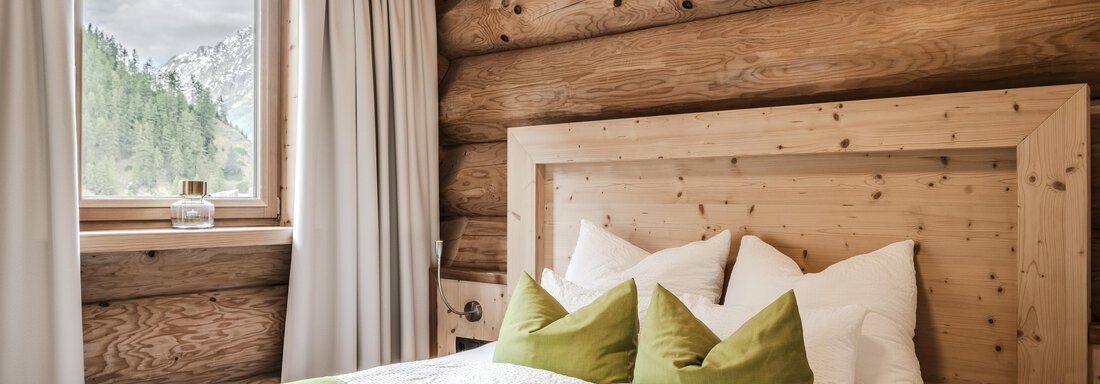 A cozy bedroom with wood paneling and large windows. Two beds with green pillows and a fresh, inviting atmosphere. - Chalet Resort Sölden - Sölden