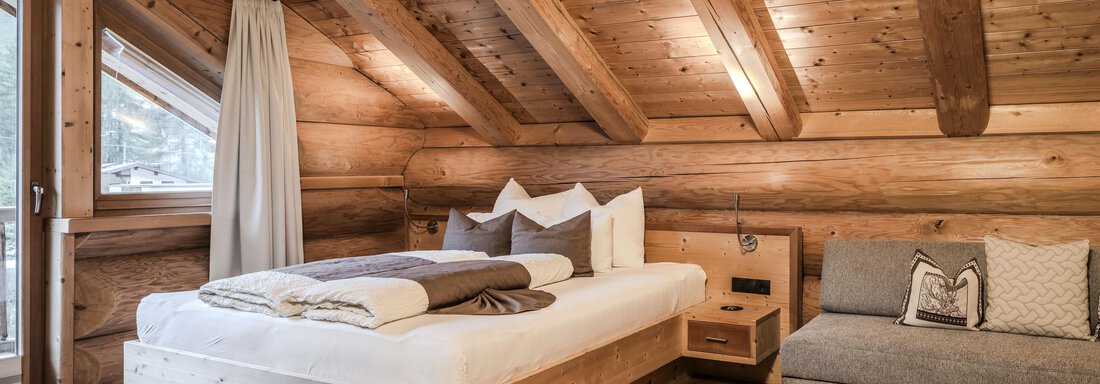 A cozy bedroom with wooden walls and a large window. The room features a large bed and a comfortable couch. - Chalet Resort Sölden - Sölden
