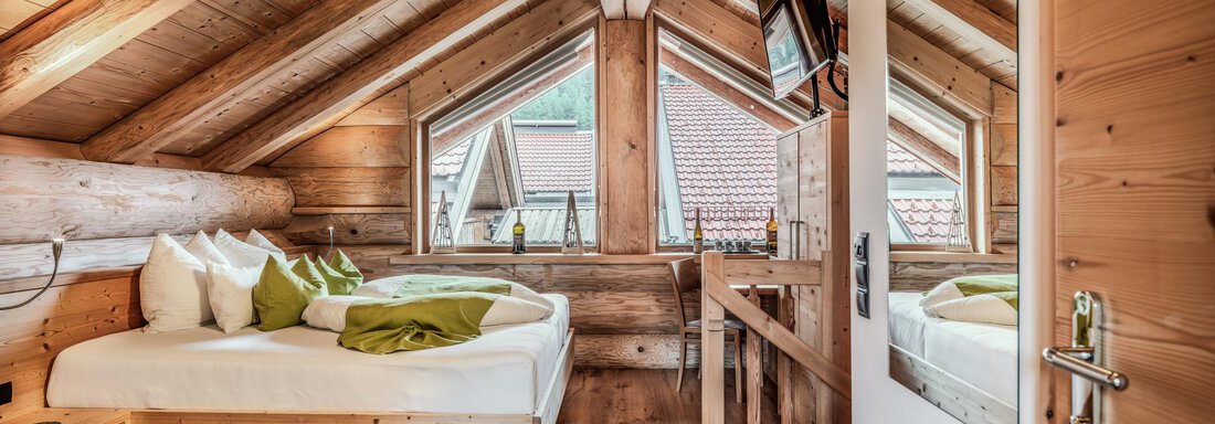 1617_Chalet_Soelden_24_185-2 - Kopie A cozy attic room with wooden walls and large windows. The room features a bed with decorative pillows and a modern vanity table. - Chalet Resort Sölden - Sölden