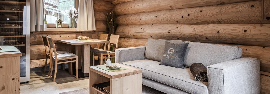 A cozy living space with wooden paneling, a bright sofa, and a small table. Daylight shines through the window, and there is a dining area with chairs. - Chalet Resort Sölden - Sölden
