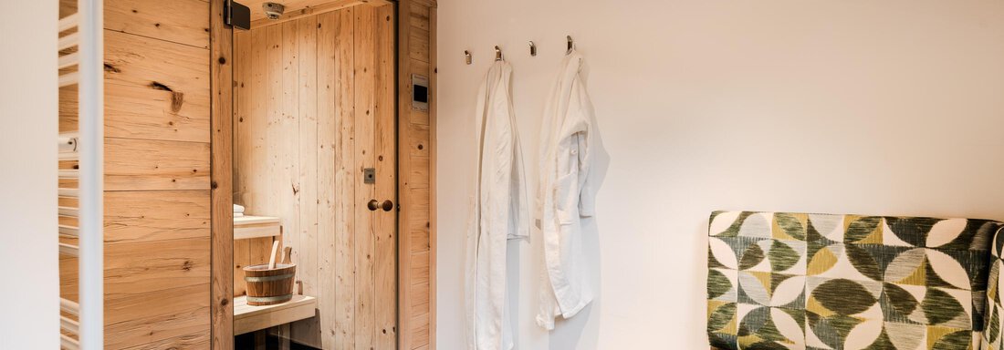 A cozy room with wooden paneling and a green sofa. There are bathrobes on the wall and an entrance to a wellness area. - Chalet Resort Sölden - Sölden