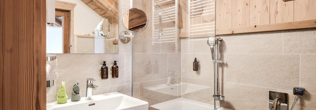 A modern bathroom with a wooden ceiling and a bathtub. It features a stylish shower and elegant wash utensils. - Chalet Resort Sölden - Sölden