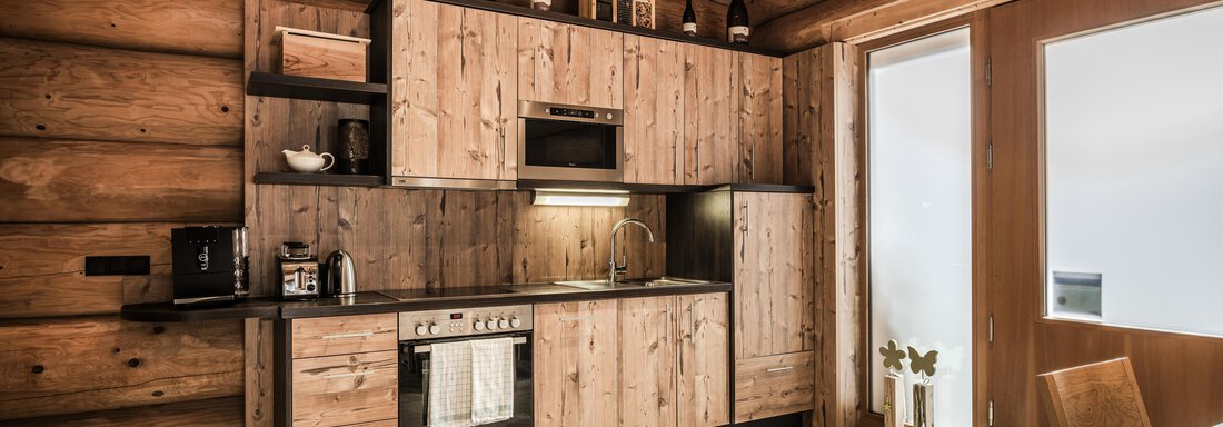 A modern kitchen with wooden furniture and elegant black accents. The large windows let in plenty of light and offer an inviting space. - Chalet Resort Sölden - Sölden