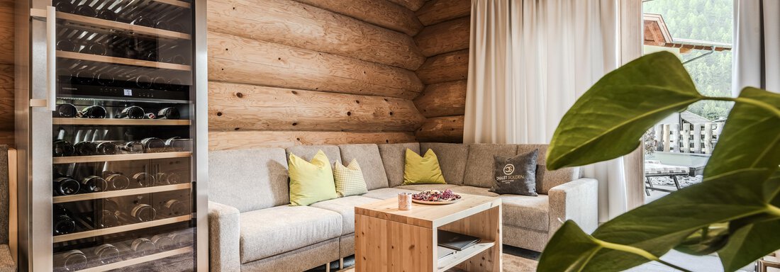 A cozy living space with wooden paneling, a comfortable sofa, and a small tabletop. A wine rack and plants give the room an inviting ambiance. - Chalet Resort Sölden - Sölden