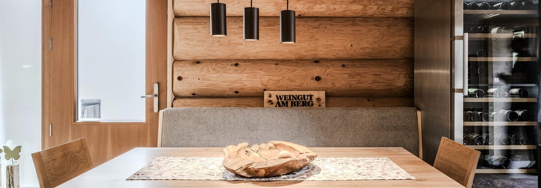 A cozy dining area with a large wooden table and four chairs. The walls are made of wood, and there is modern lighting as well as a wine cabinet. - Chalet Resort Sölden - Sölden