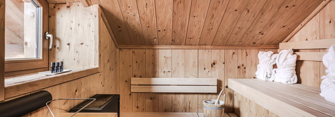 A modern sauna interior made of wood with comfortable benches and a large window. The atmosphere is relaxing and inviting. - Chalet Resort Sölden - Sölden