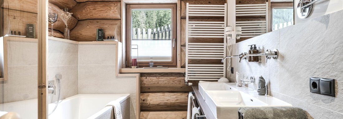 A modern bathroom with wooden walls and large windows. There is a bathtub, a sink, and a towel warmer. - Chalet Resort Sölden - Sölden