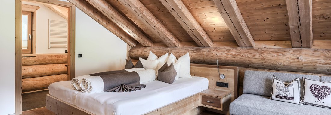 A cozy bedroom with wooden ceilings and a large bed. The decor is modern and inviting, with a gray sofa in the corner. - Chalet Resort Sölden - Sölden