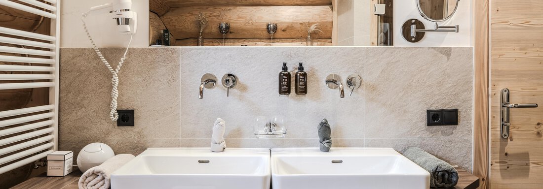A modern bathroom with two sinks and a wood theme. The decor is elegant and stylish with towels and toiletries. - Chalet Resort Sölden - Sölden