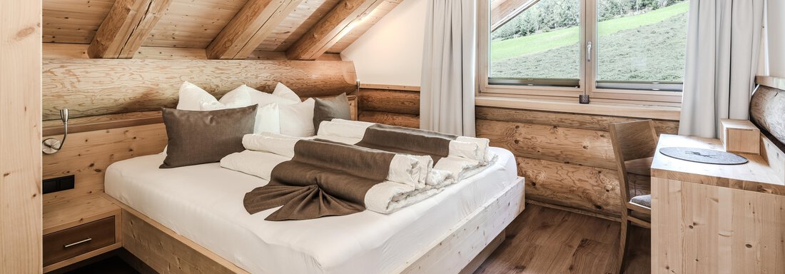 A cozy bedroom with natural wood details. There is a large window that overlooks a green environment. - Chalet Resort Sölden - Sölden