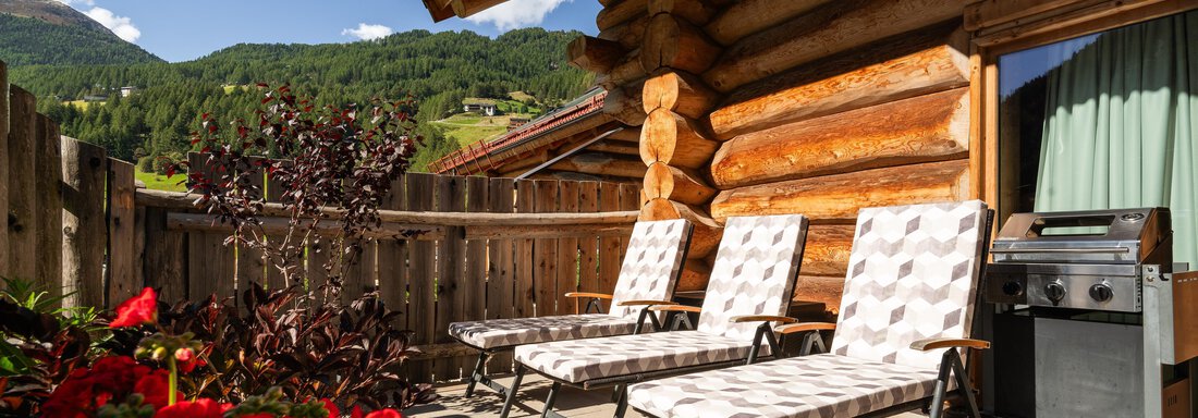 A cozy balcony with two lounges and a grill.  
Surrounded by blooming red plants and a beautiful mountain landscape in the background. - Chalet Resort Sölden - Sölden