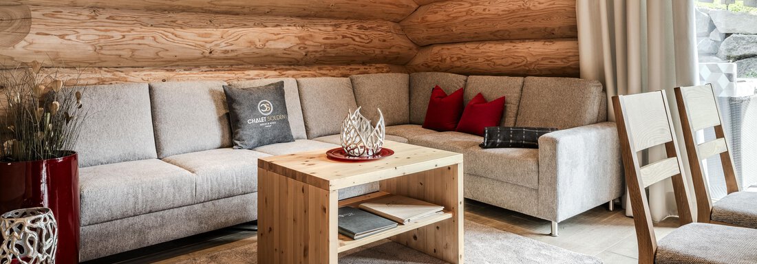 A cozy living room with bright wood paneling. A gray sofa and a wooden coffee table create an inviting atmosphere. - Chalet Resort Sölden - Sölden