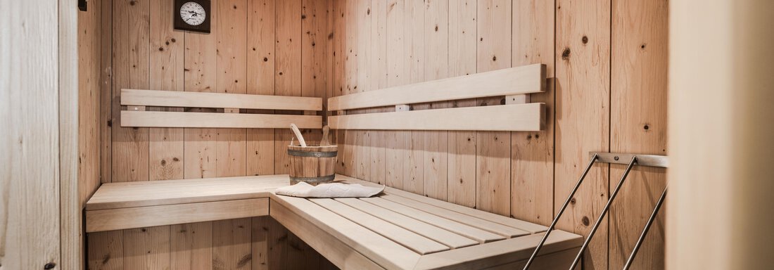 A stylish sauna with wooden paneling and benches. The relaxing atmosphere is complemented by soft lighting and a equipped corner for the sauna stove. - Chalet Resort Sölden - Sölden