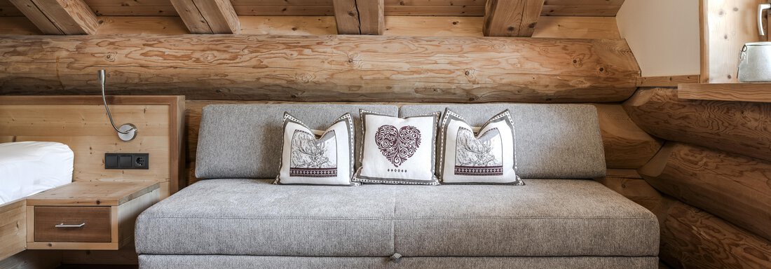 A cozy room with a gray sofa and cushions featuring heart and animal motifs. The wooden ceilings and walls give the room a warm atmosphere. - Chalet Resort Sölden - Sölden