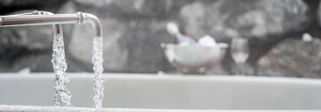 A wooden bathtub filled with bubbling water flows from a faucet. In the background, stones and an elegant vessel can be seen. - Chalet Resort Sölden - Sölden