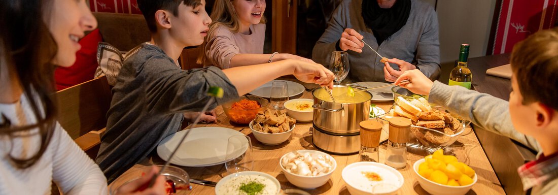 A family enjoys a shared dinner at the table. Various dishes and ingredients are visible for preparation. - Chalet Resort Sölden - Sölden