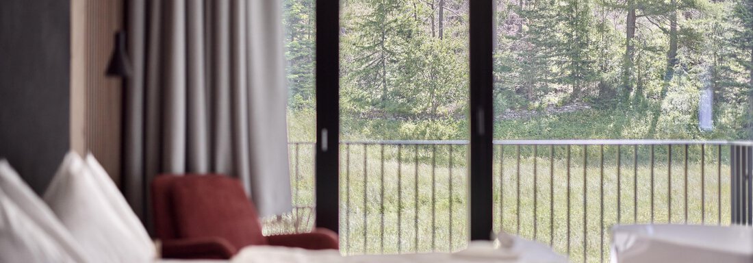 Room#2_09_web_Christoph Noesig PHOTOGRAPHY A modern bedroom with a view of a green forest. Large windows let in plenty of daylight. - Chalet White Pearl by MYALPS - Sölden