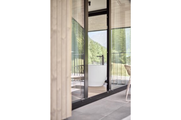 A modern bathroom with a freestanding bathtub and large windows. The view of the green landscape creates a relaxing atmosphere. - Chalet White Pearl by MYALPS - Sölden