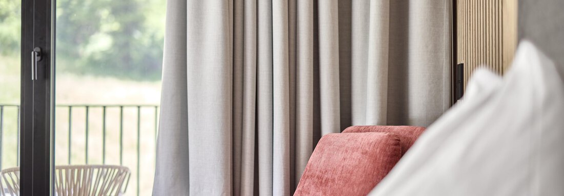 A cozy area with a red armchair and neutral curtains. The view seems to go to a balcony with a chair. - Chalet White Pearl by MYALPS - Sölden