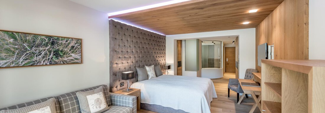 Ein modernes Hotelzimmer mit einem gemütlichen Sofa und einem großen Bett. Die Wände sind in warmen Holztönen gestaltet, und es gibt sanfte Beleuchtung. - Das Central - Alpine . Luxury . Life - Sölden