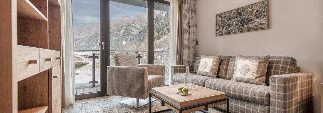 Ein gemütlicher Wohnraum mit einem modernen Sofa und einem Couchtisch. Große Fenster bieten einen Blick auf die umliegenden Berge. - Das Central - Alpine . Luxury . Life - Sölden