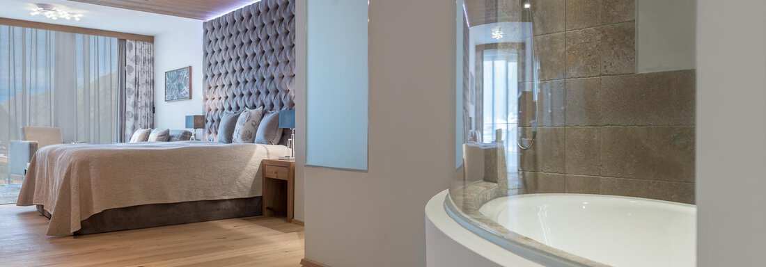 Ein modernes Schlafzimmer mit einem großen Bett und eleganten Möbeln. Im Vordergrund ist eine runde Badewanne sichtbar. - Das Central - Alpine . Luxury . Life - Sölden