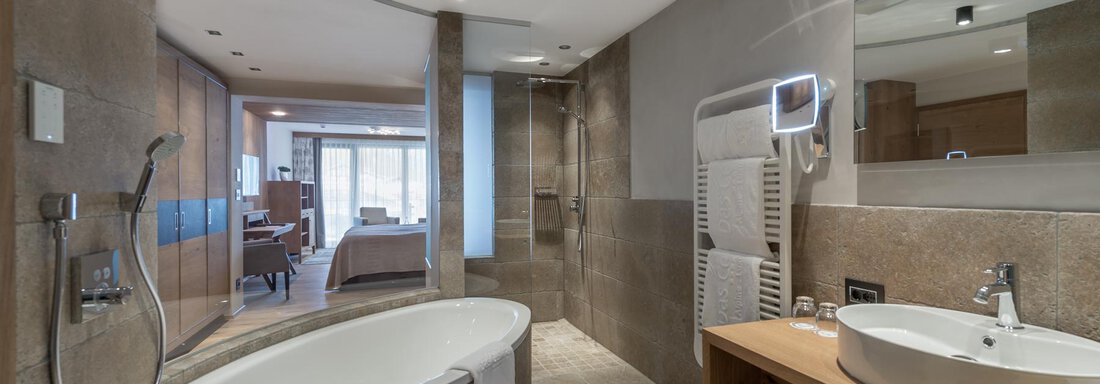 Ein modernes Badezimmer mit einer freistehenden Badewanne und einem großen Waschbecken. Die Wände sind mit eleganten Fliesen verkleidet und es gibt viel natürliches Licht. - Das Central - Alpine . Luxury . Life - Sölden