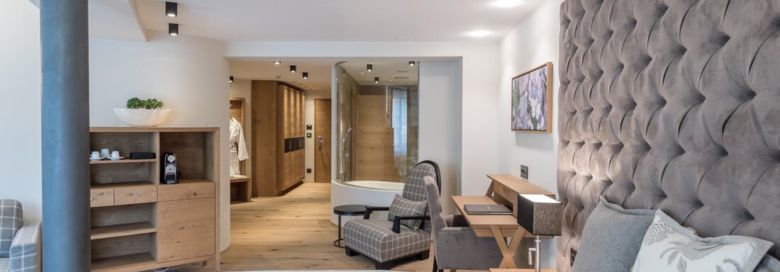 Ein modernes Schlafzimmer mit einem gepolsterten Kopfteil und einem gemütlichen Sessel. Der Raum ist hell und stilvoll eingerichtet, mit Holz- und Stoffelementen. - Das Central - Alpine . Luxury . Life - Sölden
