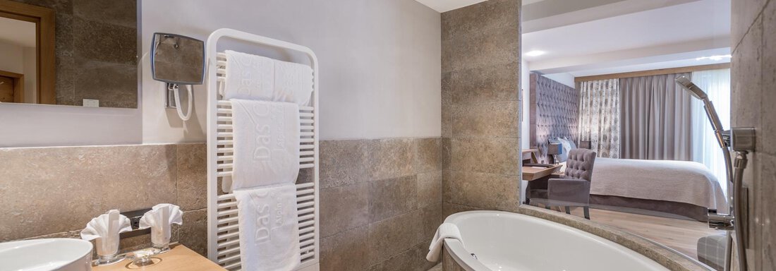 Ein modernes Badezimmer mit einer eleganten Badewanne und einem Waschbecken. Der Raum hat natürliche Steinoberflächen und viel Tageslicht. - Das Central - Alpine . Luxury . Life - Sölden