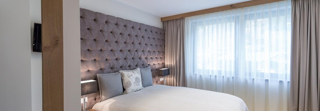Ein modernes Schlafzimmer mit einem gemütlichen Bett und einem eleganten, gepolsterten Kopfteil. Große Fenster sorgen für viel natürliches Licht. - Das Central - Alpine . Luxury . Life - Sölden