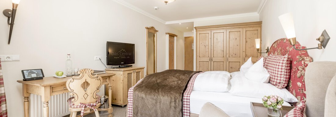 Ein elegantes Hotelzimmer mit einem gemütlichen Bett und rustikalen Holzmöbeln. Es gibt auch einen Schreibtisch und einen Fernseher im Raum. - Das Central - Alpine . Luxury . Life - Sölden