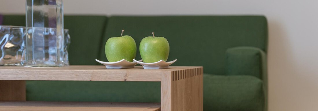 Ein modern eingerichteter Raum mit einem grünen Sofa und einem Holzkaffeetisch. Auf dem Tisch stehen zwei grüne Äpfel und eine Wasserflasche. - Das Central - Alpine . Luxury . Life - Sölden