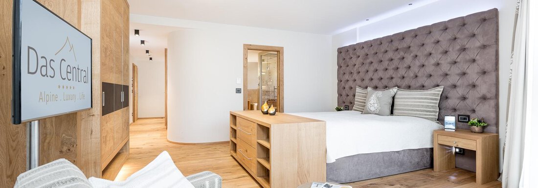 Ein modernes Hotelzimmer mit einem großen Bett und eleganter Einrichtung. Der Raum hat helle Holz- und neutrale Farbtöne für eine gemütliche Atmosphäre. - Das Central - Alpine . Luxury . Life - Sölden