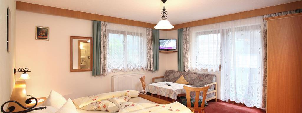A cozy room with a double bed and a small seating area. Large windows let in plenty of daylight and offer a beautiful view. - Erbhof - Sölden