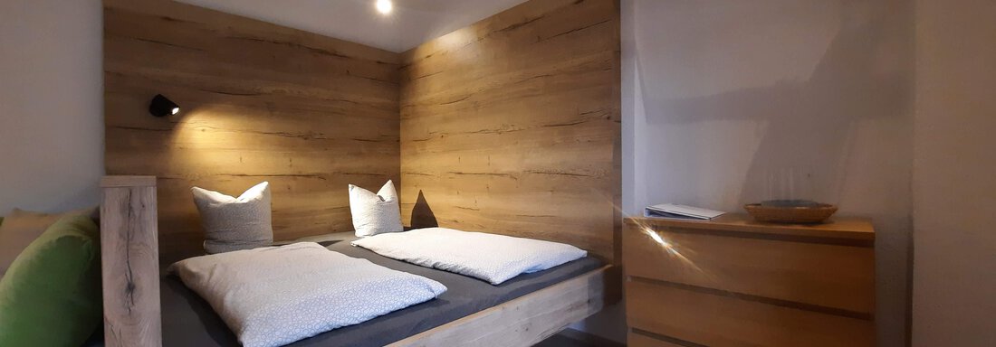 Modern bedroom with a wooden double bed and minimalist decor. The room has warm lighting and a cozy floorboard. - Ferienhaus Anna - Sölden