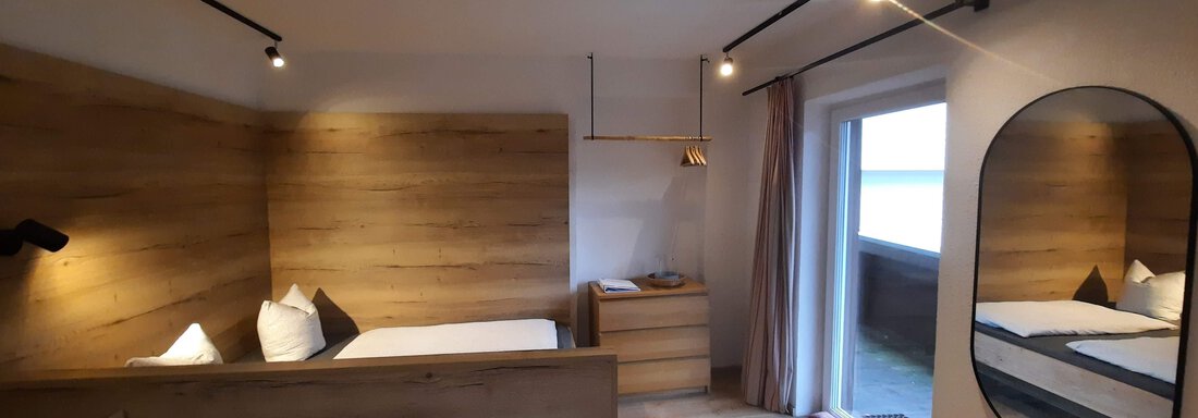A modern furnished room with wooden details and two beds. Large windows let in plenty of light and provide access to a balcony. - Ferienhaus Anna - Sölden