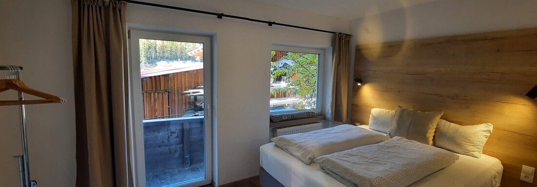 A modern bedroom with a large bed and bright curtains. The room has a balcony with a view of nature. - Ferienhaus Anna - Sölden