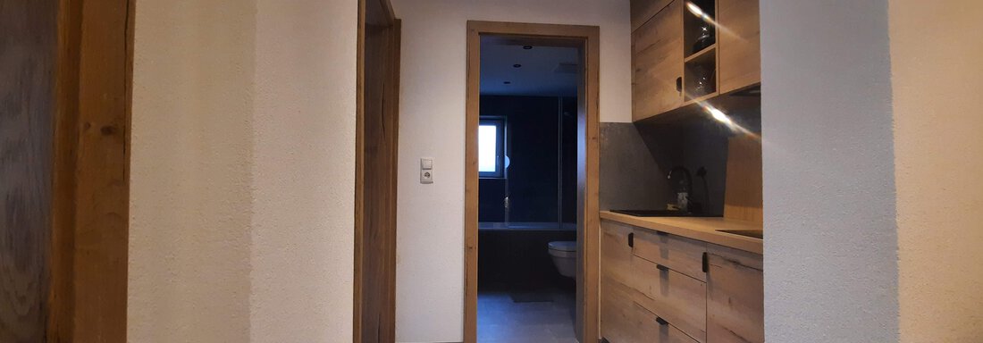 A modern hallway with wooden cabinets and a light concrete floor. The walls are plain and slightly textured. - Ferienhaus Anna - Sölden