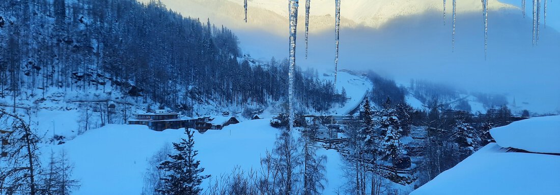 A winter landscape with snow-covered hills and trees. In the background, fog and snow-covered mountains are visible. - Ferienhaus Anna - Sölden