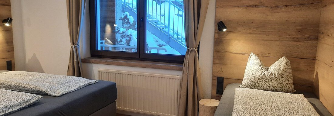 A cozy bedroom with two single beds, wooden walls, and a large window. Soft curtains and a light wood look create a relaxed atmosphere. - Ferienhaus Anna - Sölden