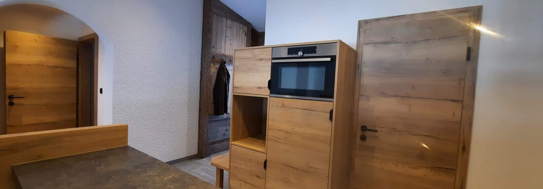 A modern kitchen with wooden cabinets and a microwave. The walls are light, and the space feels inviting and spacious. - Ferienhaus Anna - Sölden