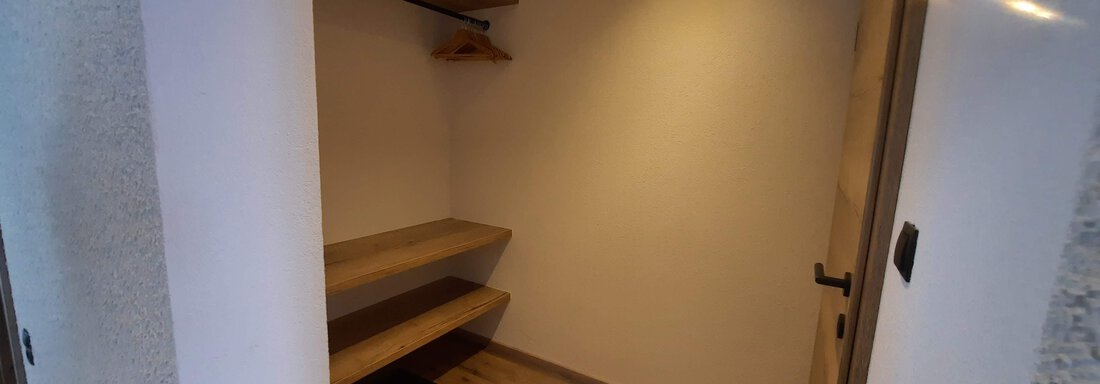 An empty room with wooden shelves and a clothes hook. The floor is made of wood, and the walls are plain and light. - Ferienhaus Anna - Sölden