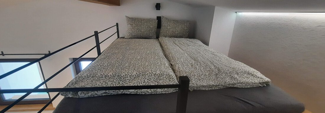 A cozy bedroom with a high bed and a modern wooden slat construction. The room has a bright and calm atmosphere. - Ferienhaus Anna - Sölden