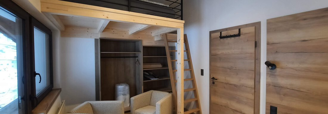 A modern room with wooden decor and a sleeping area on a loft. Two comfortable armchairs and a staircase are also visible. - Ferienhaus Anna - Sölden