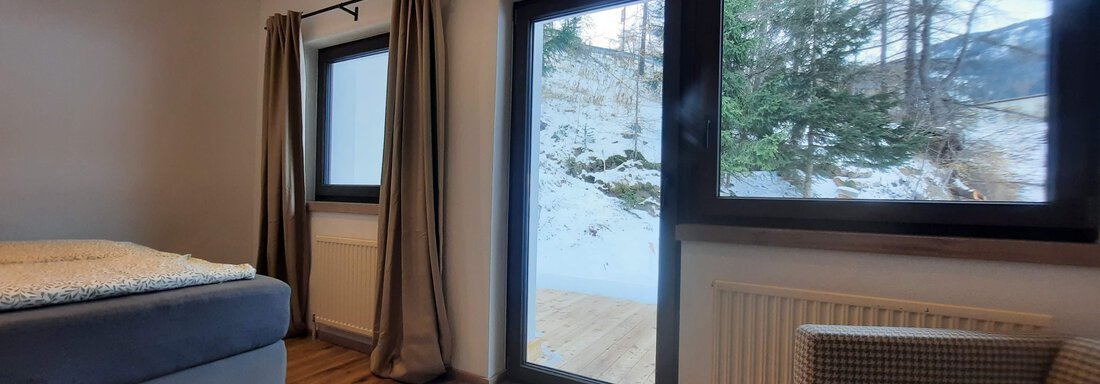 A modern bedroom with a large window and access to the terrace. The room has wooden flooring and a cozy seating area. - Ferienhaus Anna - Sölden